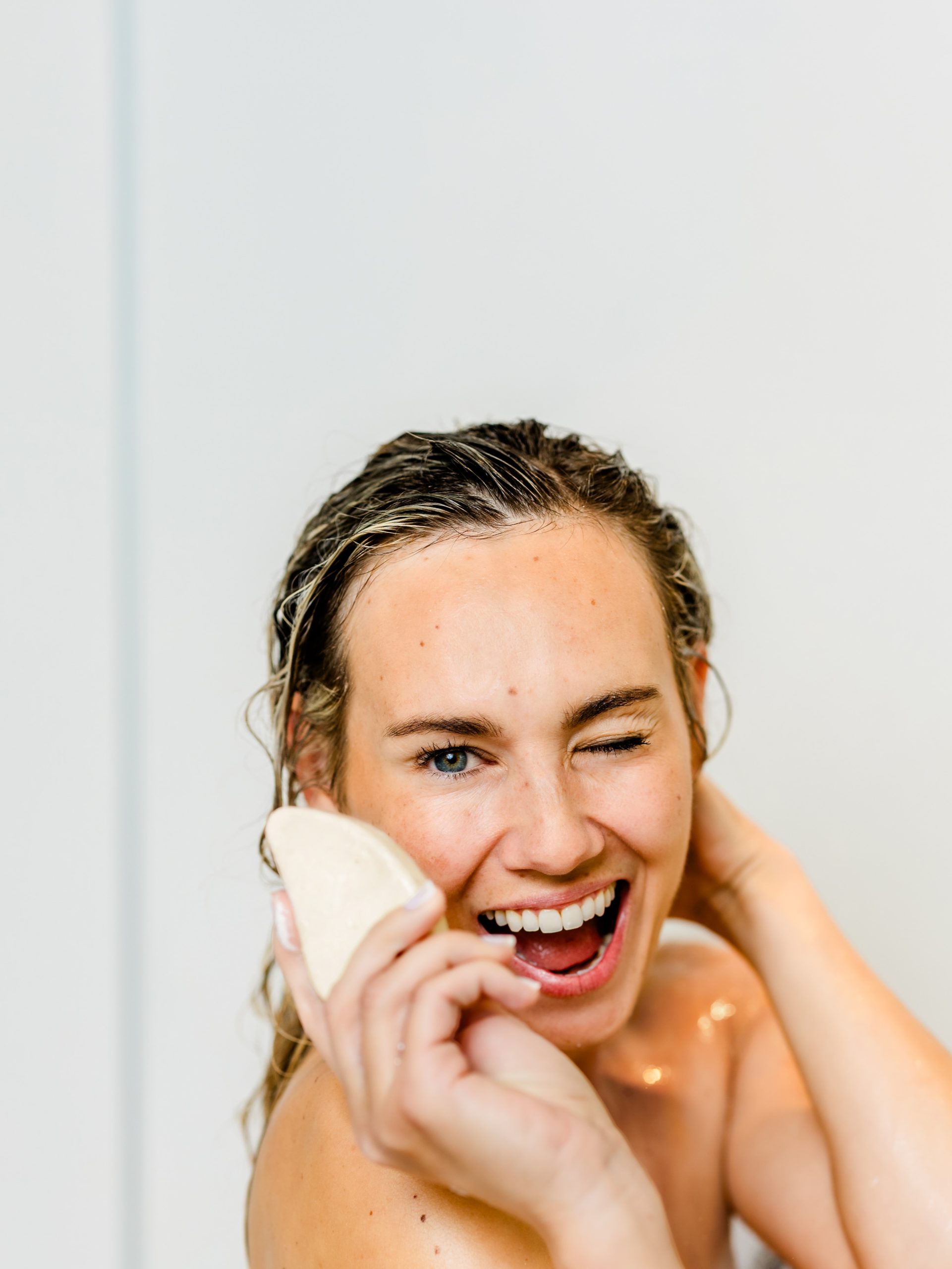 Eine lachende Frau hält das feste Hyaluron Shampoo von INUANA für die nachhaltige Haarpflege in der Hand.