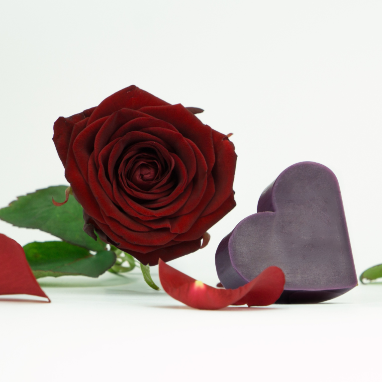 Herzförmige dunkelviolette Seife von INUANA neben einer roten Rose als pflegendes Kosmetik-Produkt für die Körperpflege.