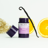 Geöffneter INUANA Haarwax Stick Nectarine und Musk dekoriert mit Orangenscheiben und einer Vanilleschote für die Haarpflege.