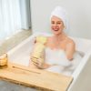 Eine lächelnde Frau in der Badewanne trägt eine gelbe Körperpflege von INUANA auf ihr Bein auf.