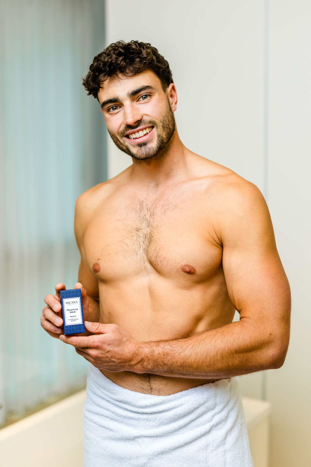 Lächelnder Mann zeigt die Umverpackung vom Haarwax Stick Signature als Kosmetik Stick von INUANA