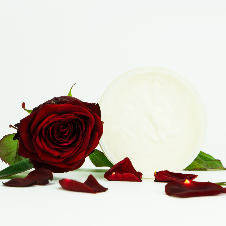 Zucker-Körperpeeling 2in1 Violette Noire von INUANA neben einer roten Rose und verstreuten Blütenblättern.