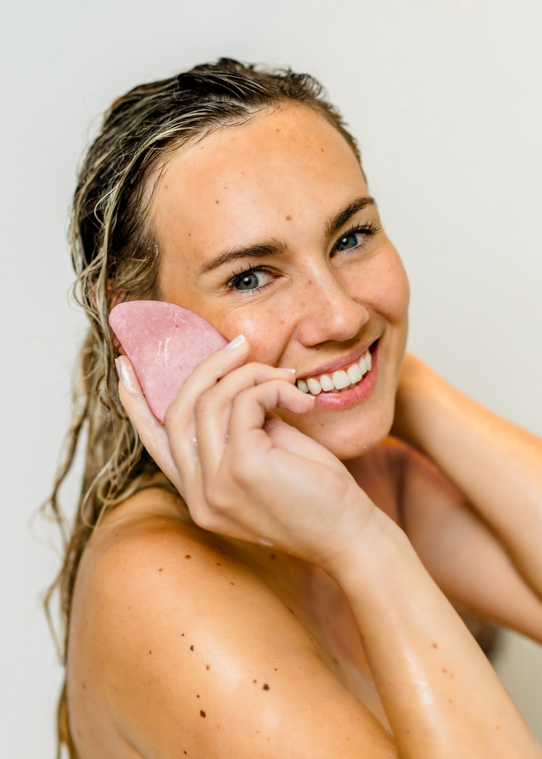 Lächelnde Frau wendet ein festes Shampoo von INUANA im nassen Haar an für eine sanfte Haarpflege.