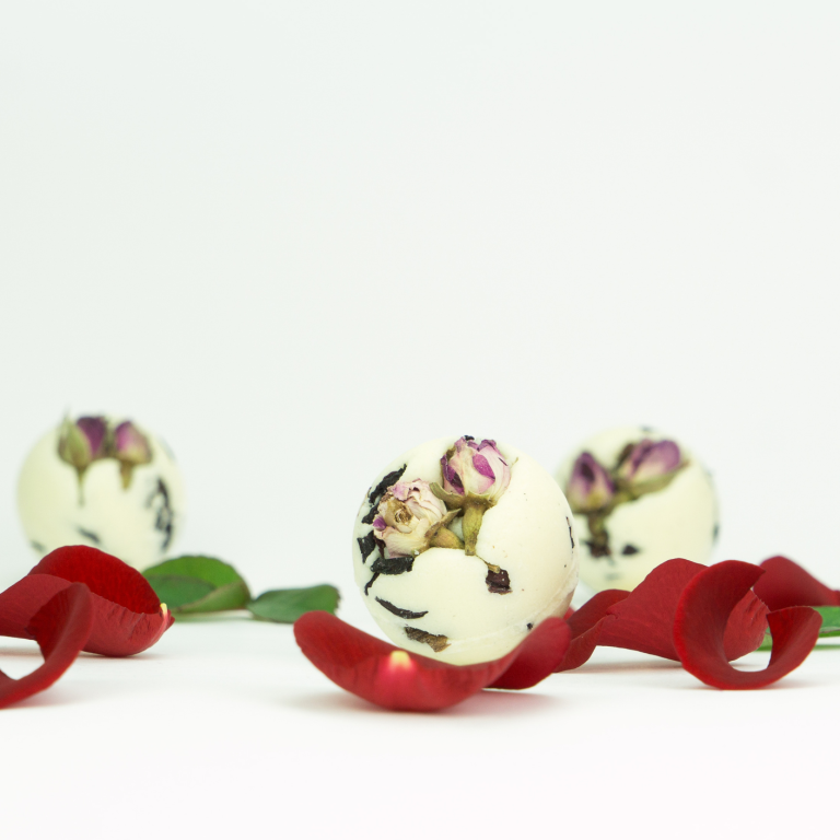Drei runde INUANA Badekugel mit Rosenblüten als natürlicher Badezusatz umgeben von roten Blütenblättern