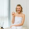 Lächelnde Frau im weißen Handtuch hält eine INUANA Badekugel Cedarwood & Orange als Badezusatz