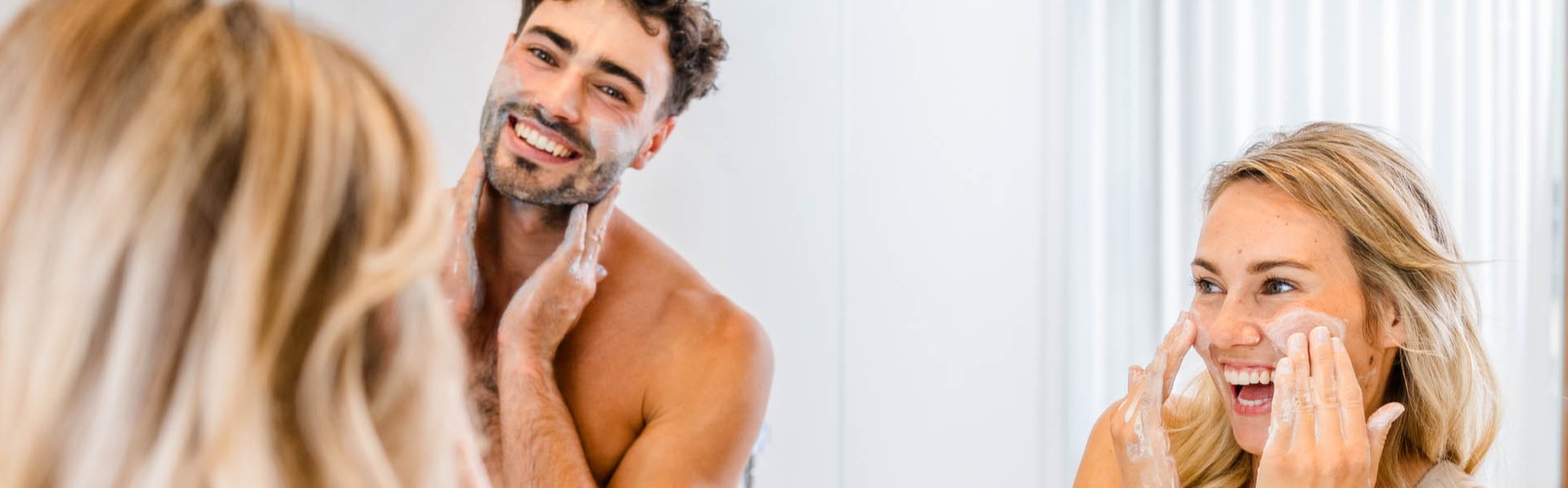 Zwei Personen lachen beim Auftragen von Gesichtspflege von Inuana vor dem Badezimmerspiegel.