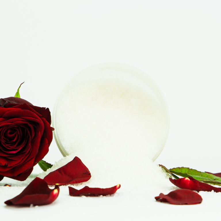 Badesalz mit roten Rosenblüten und einer frischen Rose als dekorativer Badezusatz von INUANA