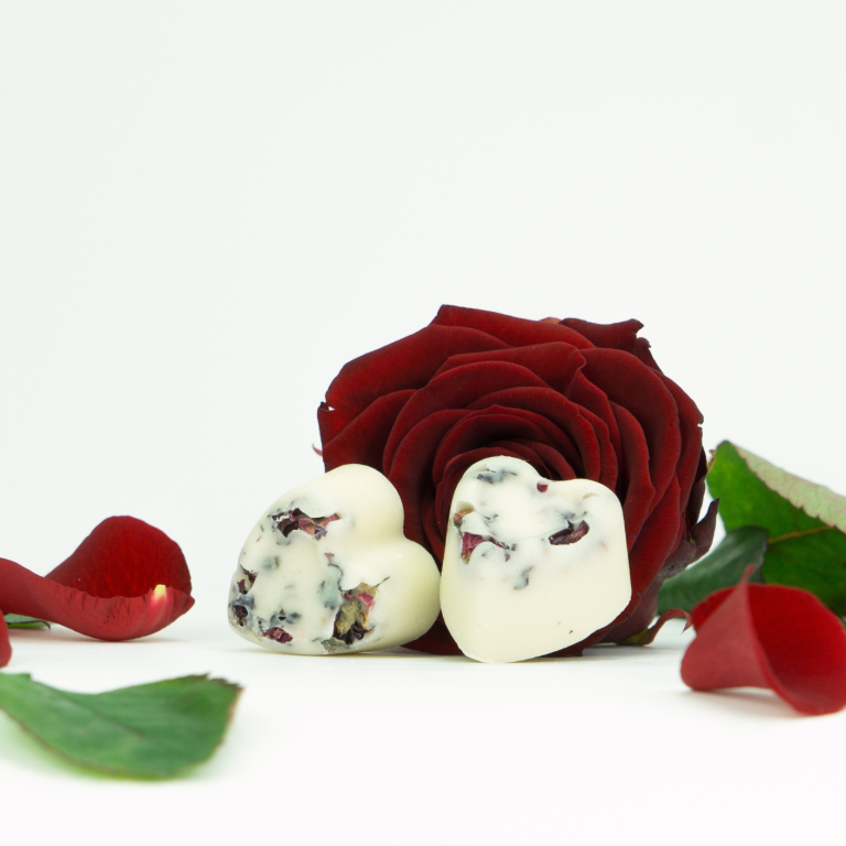 Feste Seife in Herzform mit natürlichen Inhaltsstoffen vor dunkelroter Rose von INUANA