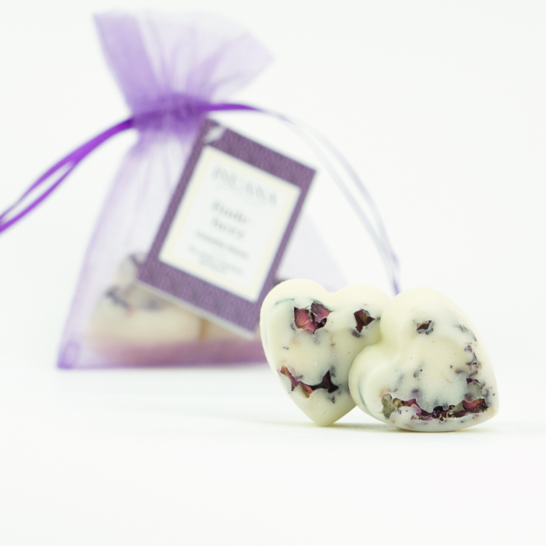 Zwei herzförmige Badeherzen als natürlicher Badezusatz vor einem violetten Organzabeutel von INUANA