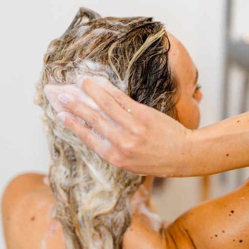 Eine Person schäumt ihr blondes Haar beim Duschen mit einem festen Shampoo von INUANA ein.