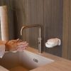 Eingeseifte Hände am Waschbecken neben einem weißen INUANA Wanddispenser für pflegende Seife.