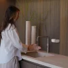 Frau wäscht ihre Hände am Waschbecken mit Seife neben dem weißen INUANA Wanddispenser.