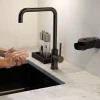 Eingeseifte Hände am Spülbecken neben einem schwarzen INUANA Wanddispenser für sanfte Körperpflege.
