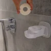 Hand hält runde feste Seife über weißem INUANA Wanddispenser an Fliesenwand für Duschpflege.