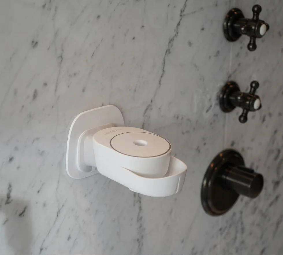 Weißer Wand-Seifenspender von INUANA an einer hellem Marmorwand in der Dusche für sanfte Duschpflege.