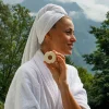 Frau im Bademantel hält eine feste runde Seife von INUANA für nachhaltige Duschpflege im Freien.