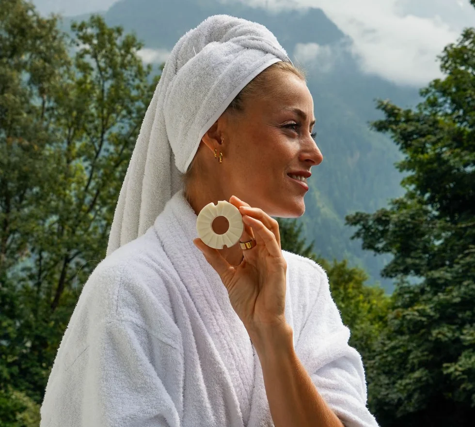 Frau im Bademantel hält eine feste runde Seife von INUANA für nachhaltige Duschpflege im Freien.